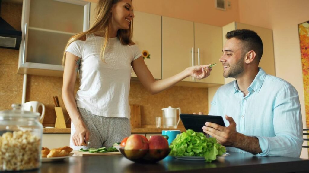 Attractive couple chatting in the kitchen early morning. Beautiful woman feed her husband while cooking breakfast at home
